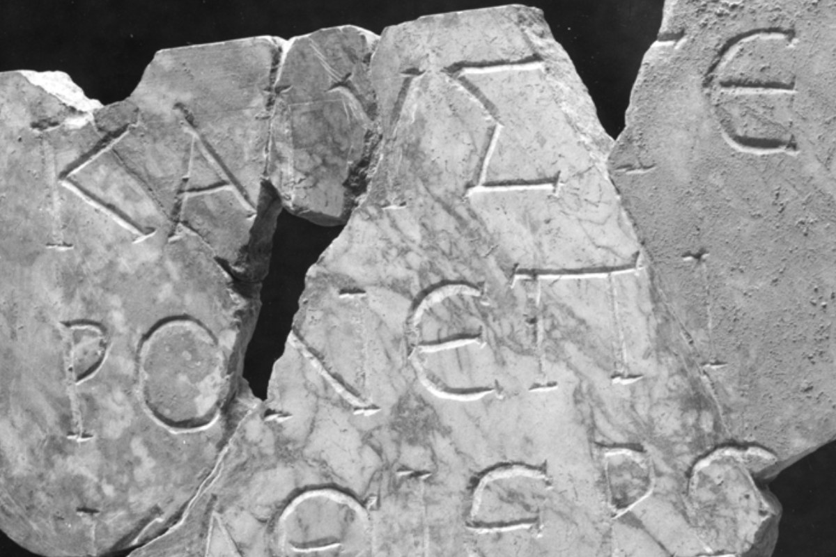 A fragmented ancient Greek inscription carved into marble, with bold letters etched into the weathered stone surface.